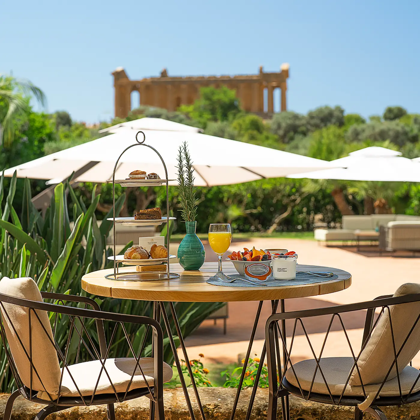 Tavolo all'aperto del Ristorante Federico II apparecchiato per la colazione con dolci, frutta e spremuta, vista sul tempio della Valle dei Templi.