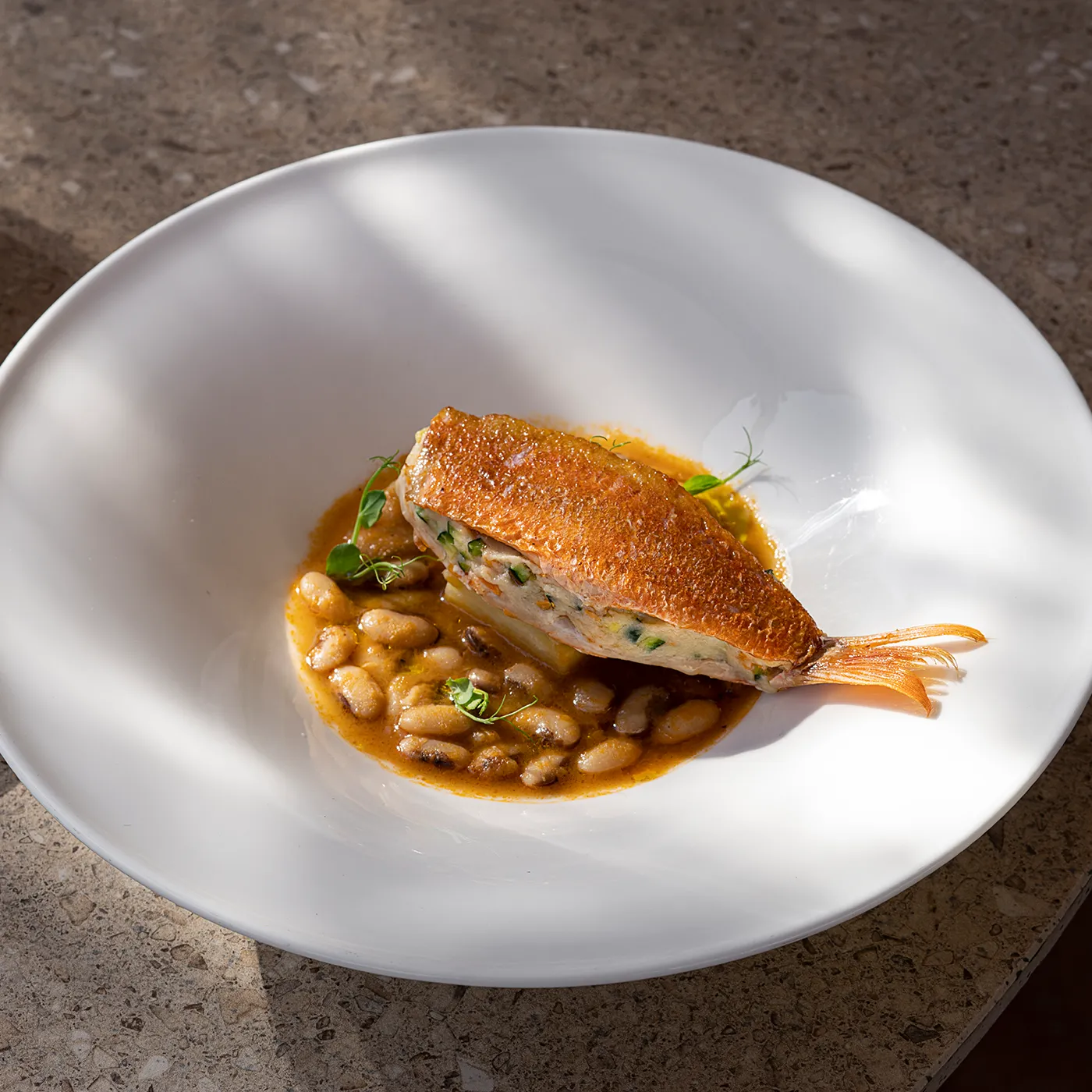 Piatto gourmet del Ristorante Federico II con filetto di triglia ripieno adagiato su una crema di fagioli, servito in un piatto fondo bianco.