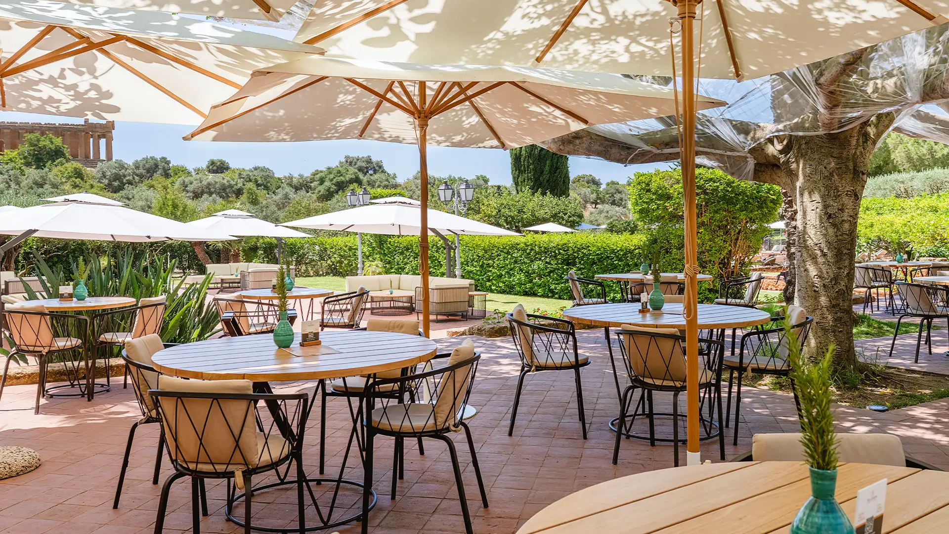Terrazza all'aperto del Ristorante Federico II allestita con tavoli in legno, ombrelloni chiari e vista sul tempio della Valle dei Templi.