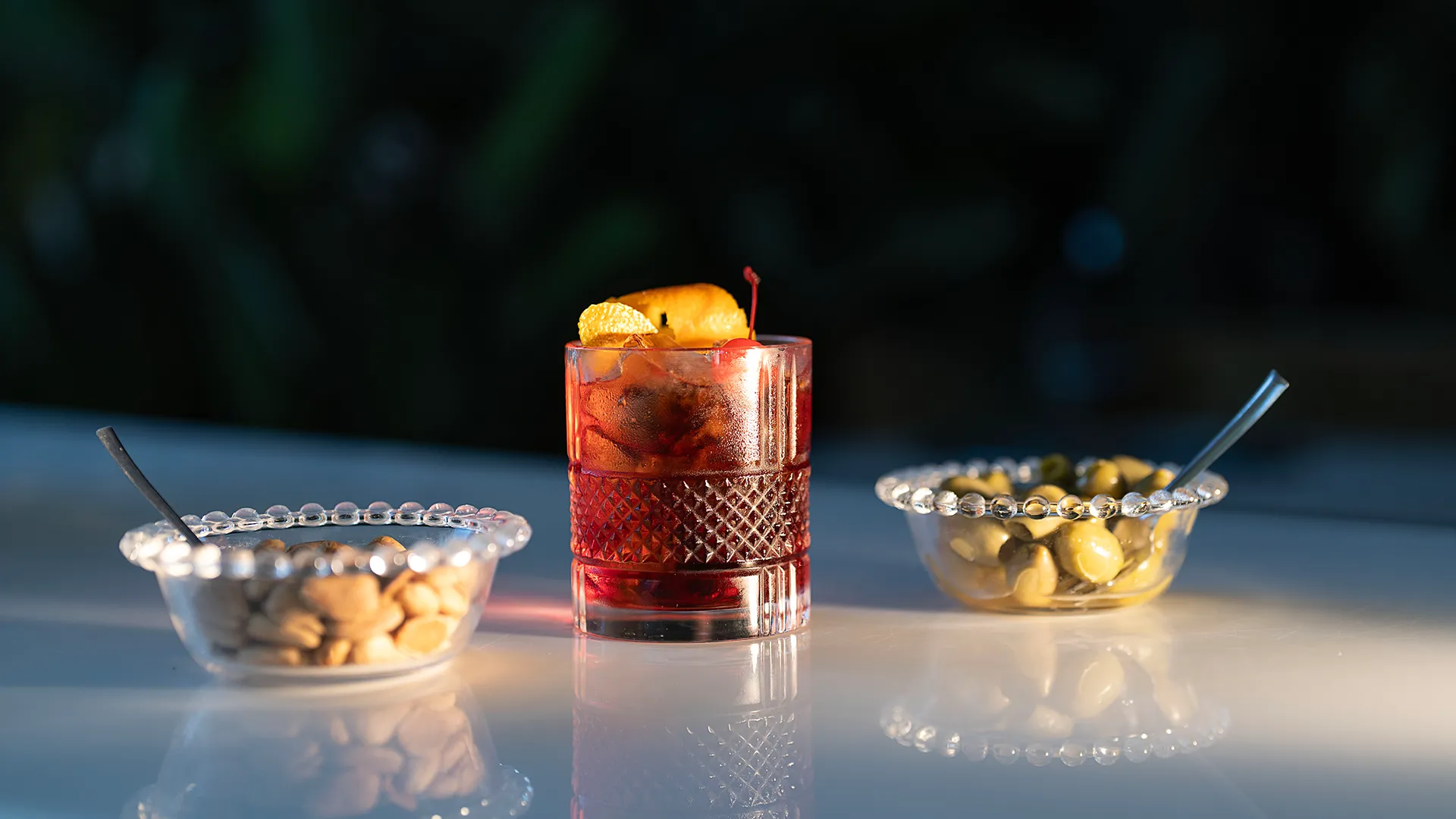 Cocktail Negroni servito in bicchiere lavorato con scorza d'arancia, accompagnato da ciotole di olive e arachidi al Ristorante Federico II.